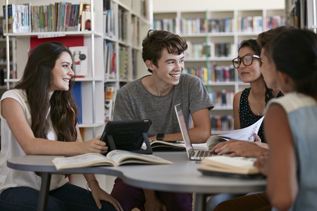 Four teenagers sitting in a library talking to each other.
